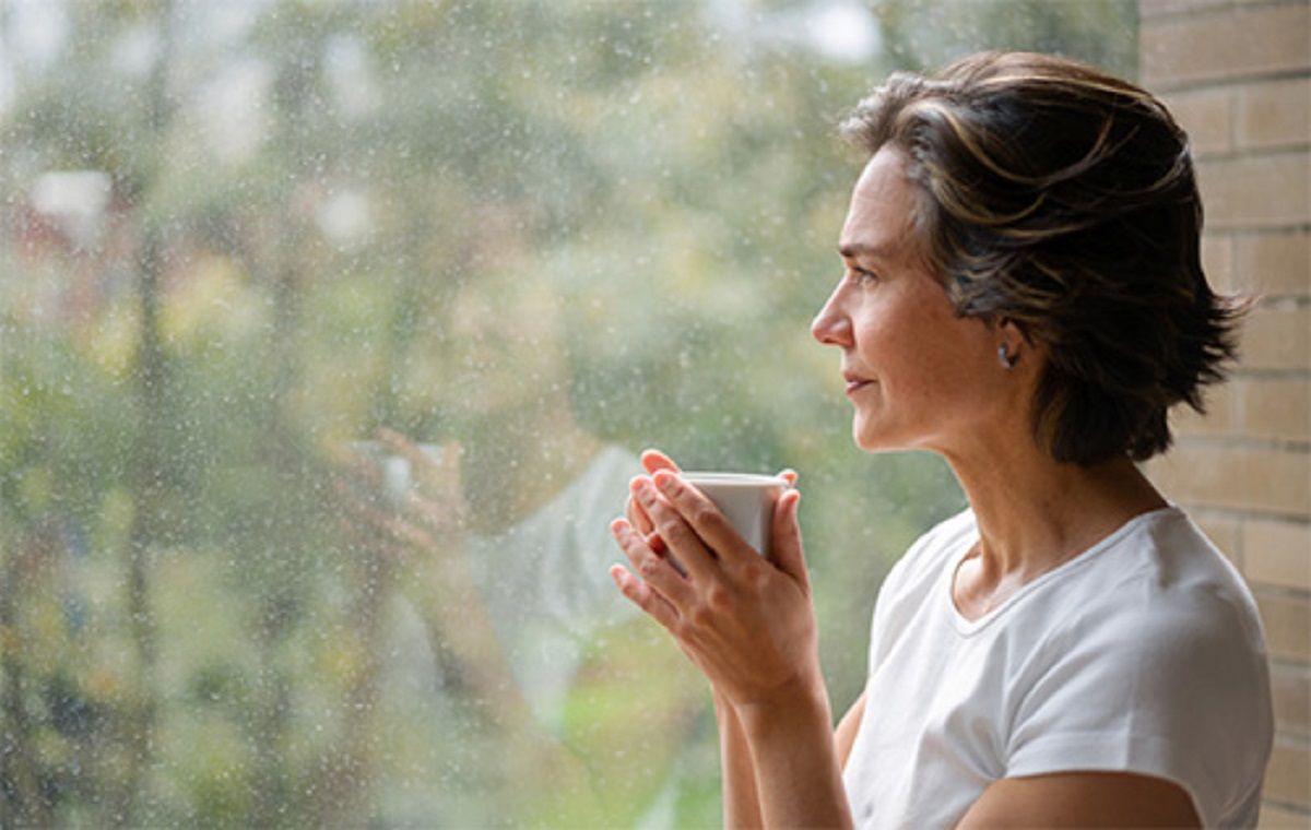 Femeie aflata la menopauza care se uita pe geam
